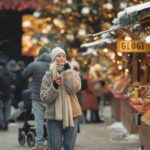 Laponia – przewodnik turystyczny po północy Finlandii Kobieta stoi ciepło ubrana i trzyma drinka na tętniącym życiem jarmarku bożonarodzeniowym.