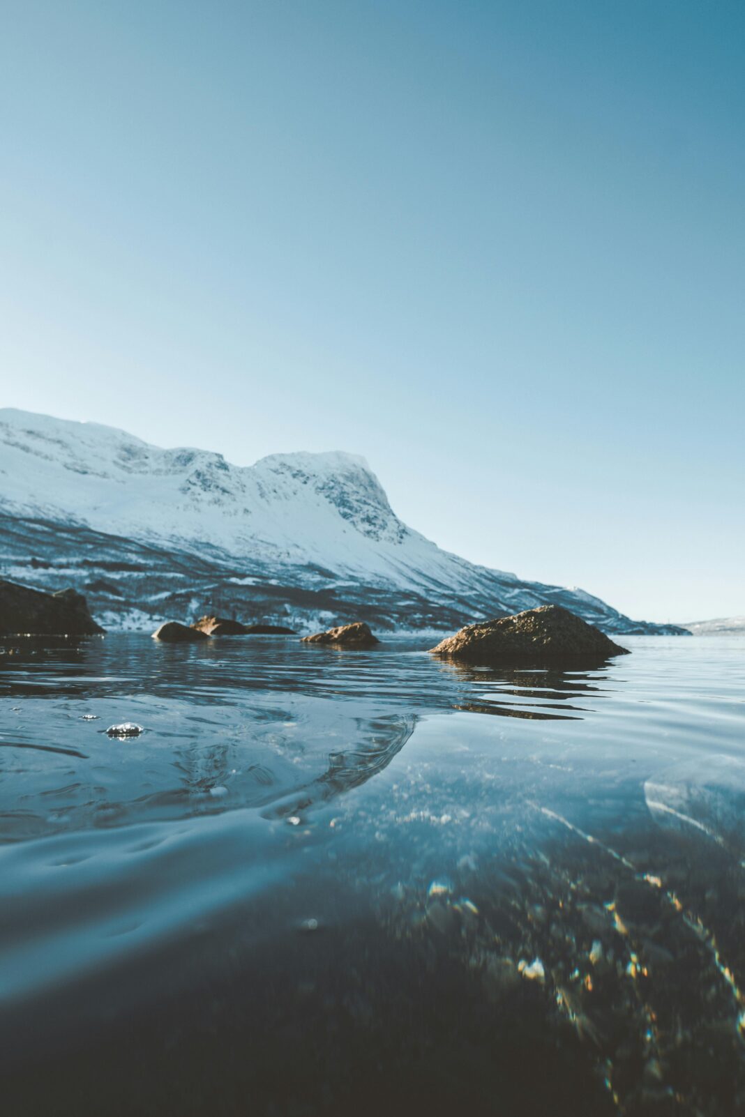 finlandia Spokojny zimowy krajobraz z zamarzniętym jeziorem i pokrytymi śniegiem górami pod czystym niebem.
