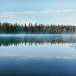 Spokojne fińskie jezioro odzwierciedla las i poranną mgłę o wschodzie słońca.