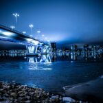 Tętniący życiem niebieski pejzaż miejski z nowoczesnym oświetlonym mostem odbitym nocą w spokojnych wodach.