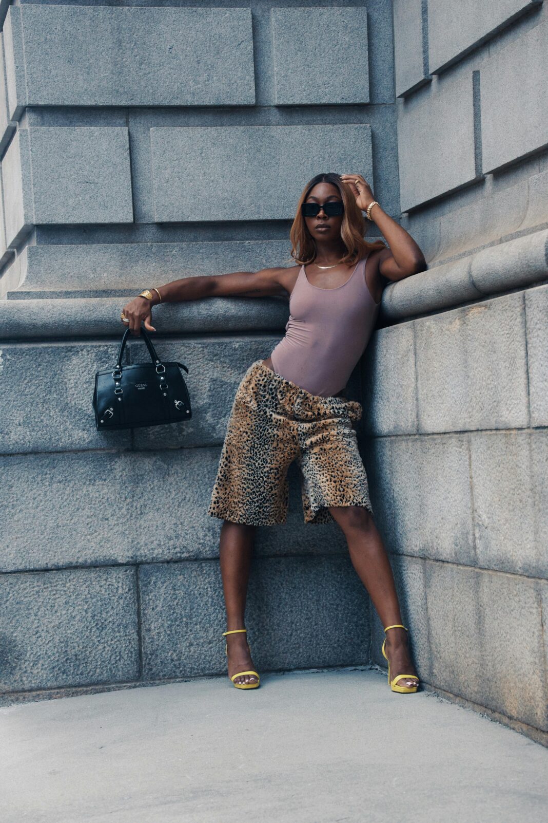gujana Modna kobieta pozuje na tle zabudowy miejskiej, ubrana w szorty z nadrukiem geparda i żółte obcasy, emanująca pewnością siebie.