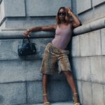 Złota gorączka w Gujanie: Historia i teraźniejszość Modna kobieta pozuje na tle zabudowy miejskiej, ubrana w szorty z nadrukiem geparda i żółte obcasy, emanująca pewnością siebie.