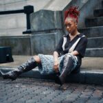 Młoda kobieta o rudych włosach siedząca na ulicy Georgetown prezentuje nowoczesną modę miejską.