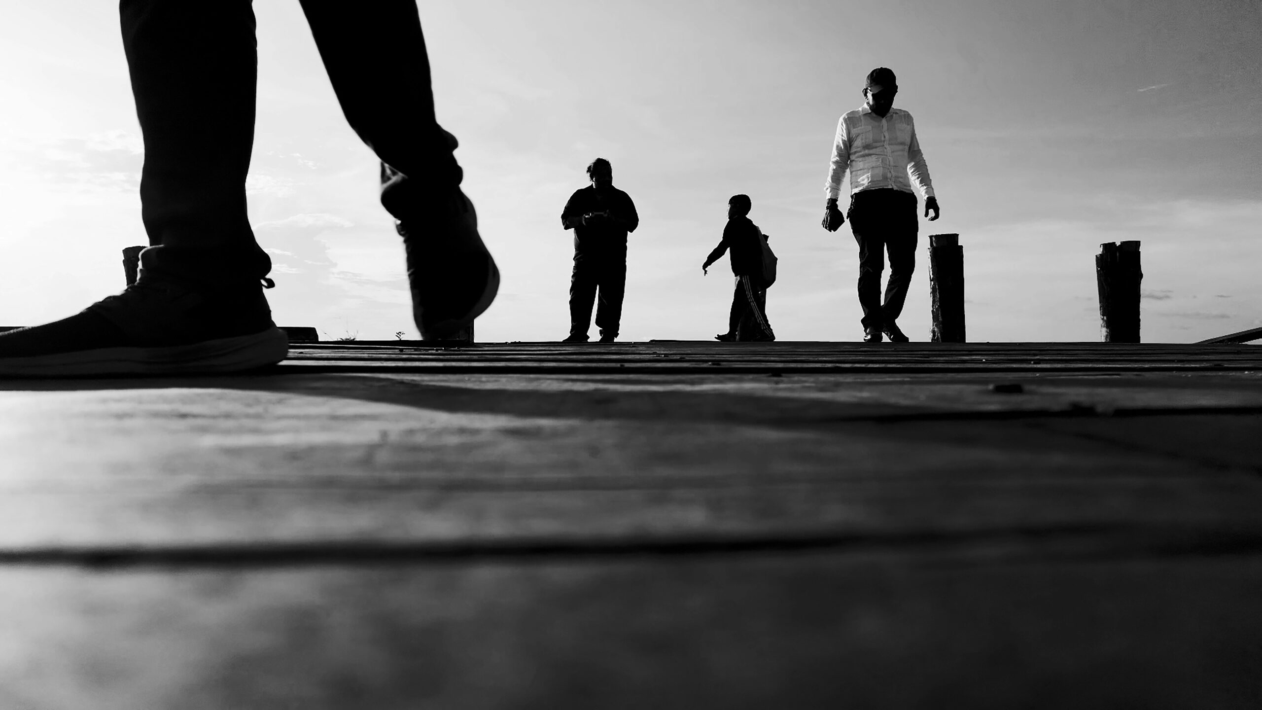Czarno-białe ujęcie sylwetek ludzi spacerujących po nabrzeżu w Georgetown o zachodzie słońca.