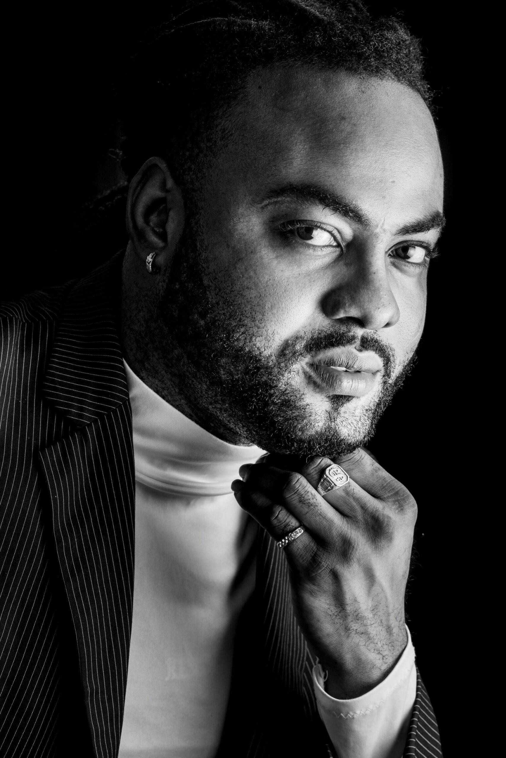 Stylowy, monochromatyczny portret przedstawiający pewnego siebie brodatego mężczyznę w garniturze o zamyślonym wyrazie twarzy.