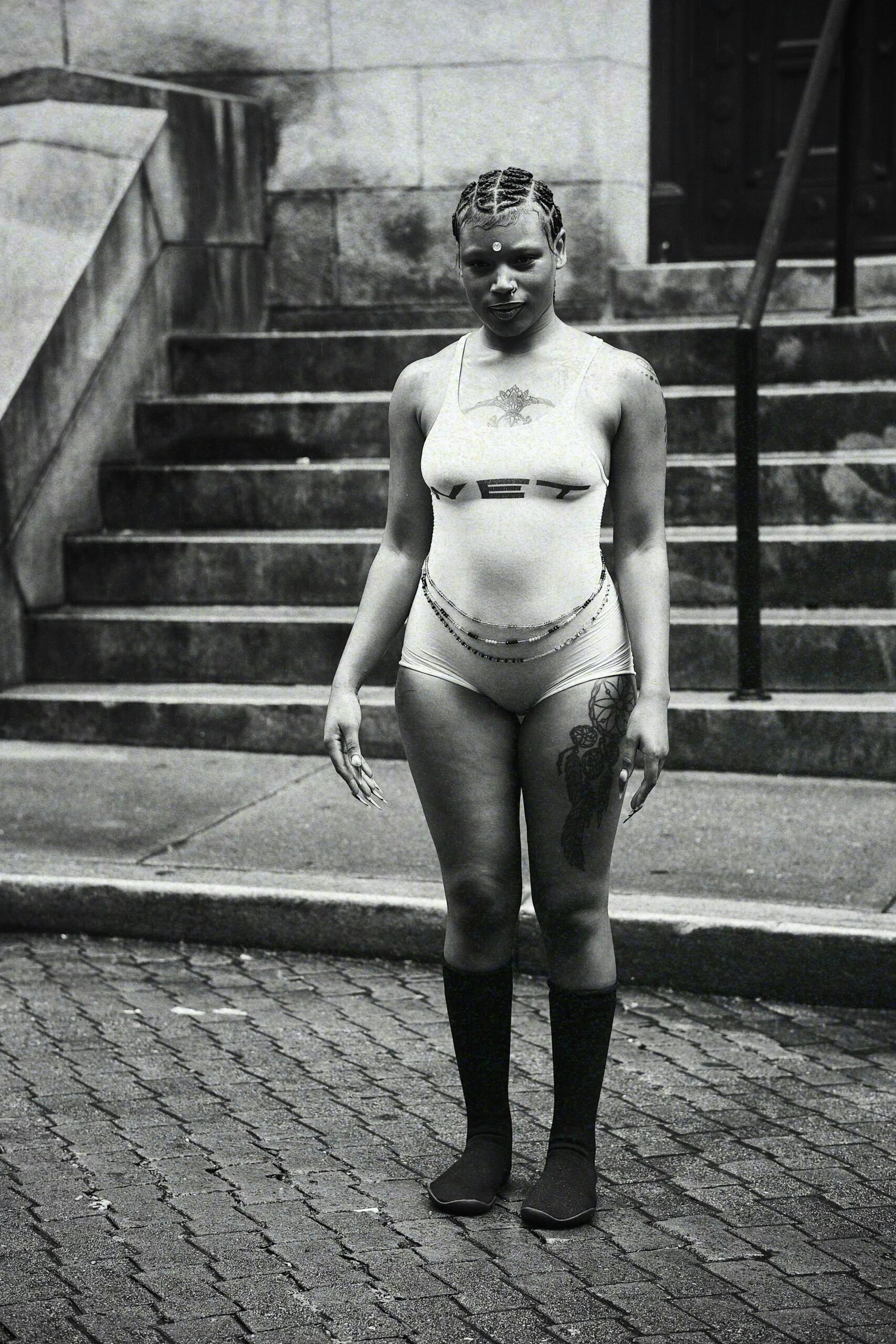 Artystyczny czarno-biały portret kobiety w miejskiej modzie, przedstawiający tatuaże na ciele i pewną siebie pozę.