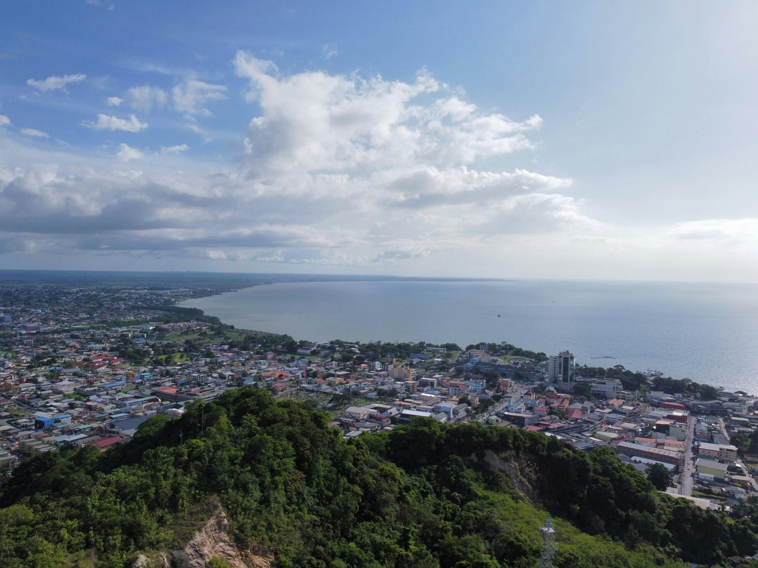 Zdjęcia lotnicze tętniącego życiem nadmorskiego miasta otoczonego bujną zielenią i spokojnym morzem pod jasnym niebem.