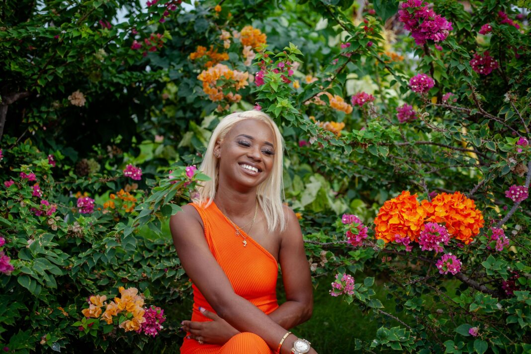 Żywy portret uśmiechniętej kobiety w kolorowym ogrodzie, emanującym radością i letnim klimatem.