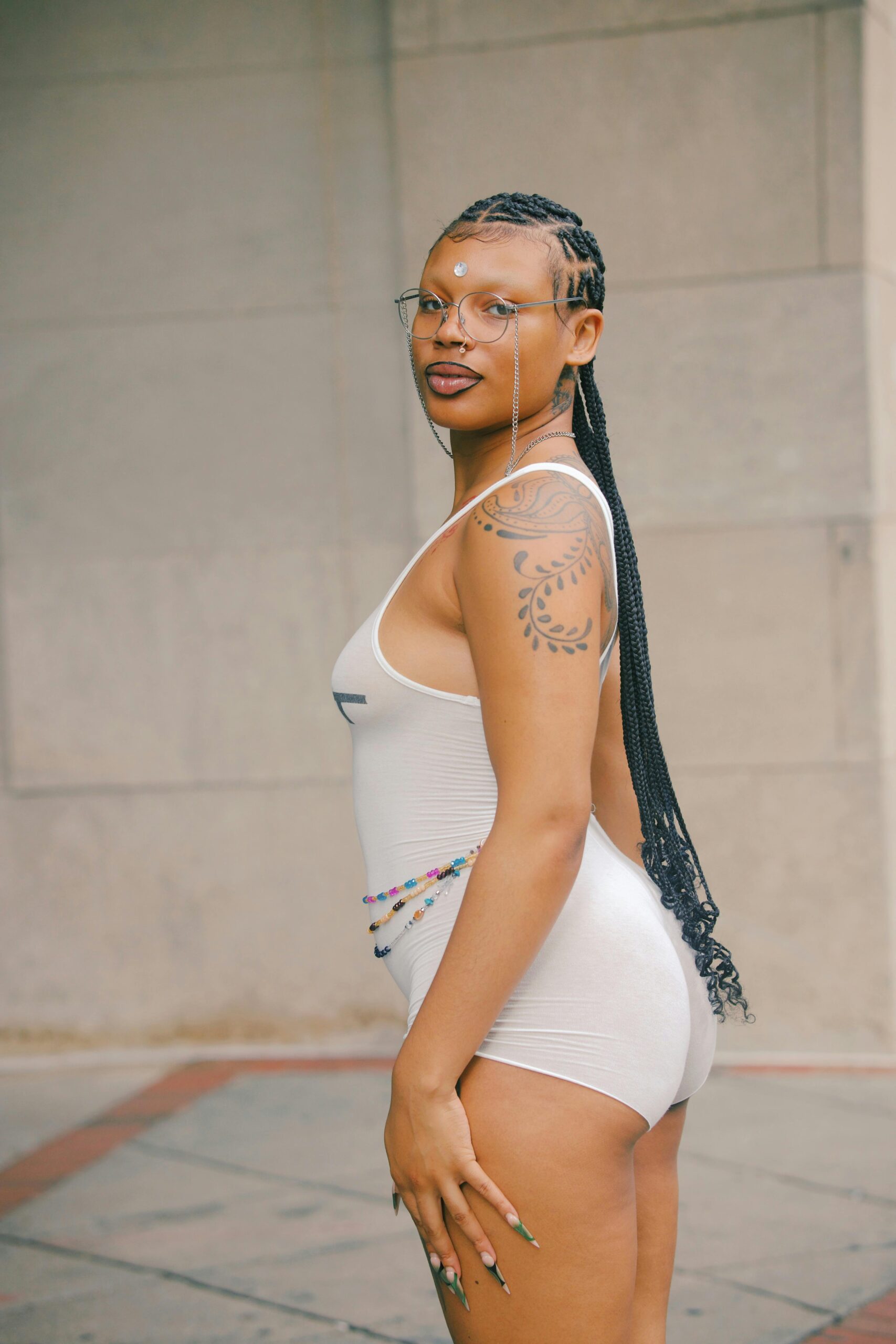 Pewna siebie kobieta w białym stroju pozująca na świeżym powietrzu, prezentująca modę i tatuaże.