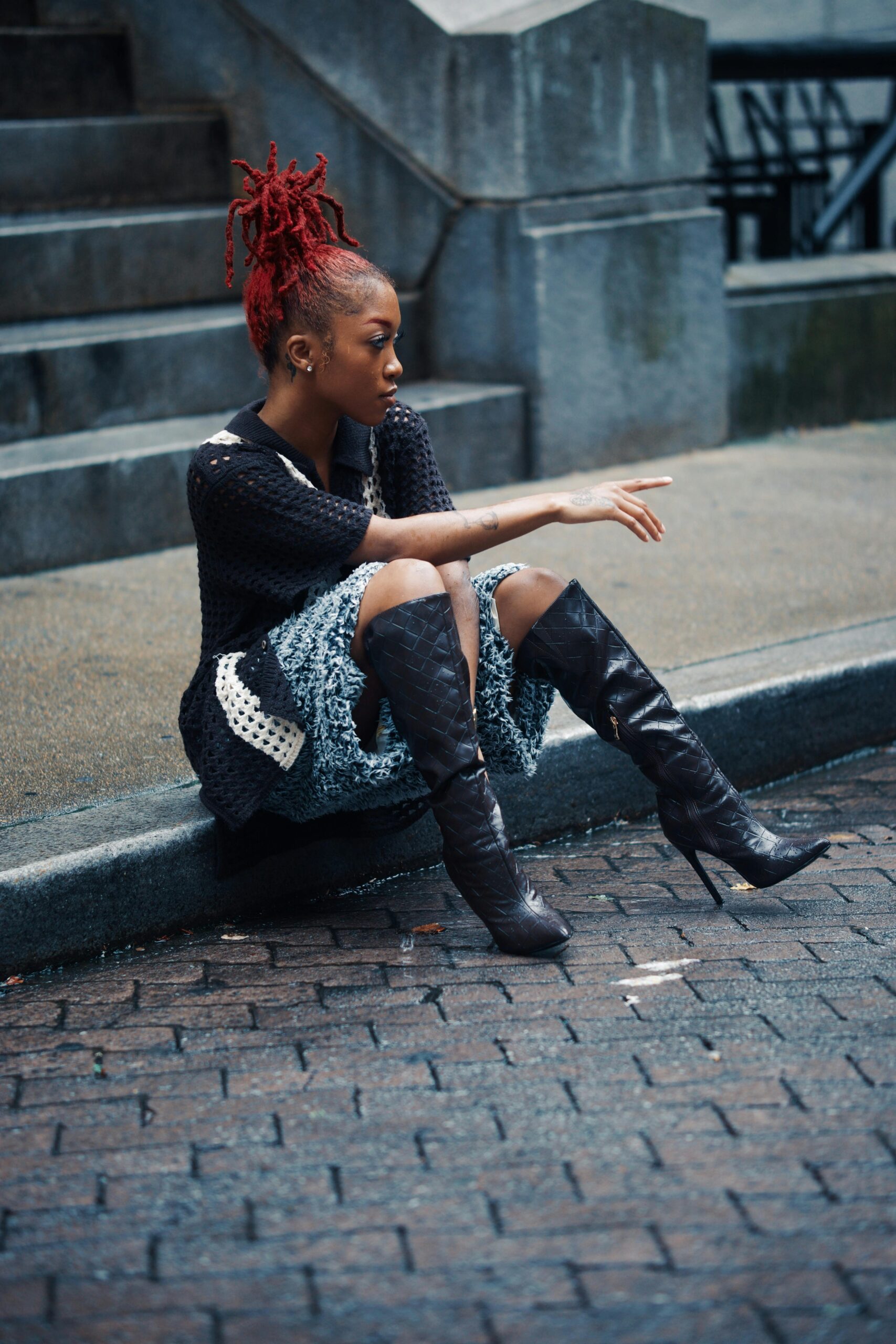 Stylowa kobieta z rudymi włosami siedzi na schodach na zewnątrz i prezentuje miejską modę.