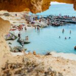 Najpiękniejsze zabytki na Majorce. Malownicza plaża w Hiszpanii z ludźmi lubiącymi pływać i opalać się przy formacjach skalnych.