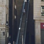 Schody ruchome między nowoczesnymi budynkami w Lleida w Hiszpanii, z ludźmi korzystającymi z nich w słoneczny dzień.