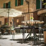 Urocza kawiarnia na świeżym powietrzu na Majorce w Hiszpanii, z żelaznymi krzesłami i rustykalnymi kamiennymi budynkami.