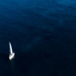 Samotna żaglówka płynie po rozległym, błękitnym oceanie pod czystym niebem.