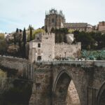 Majestatyczny widok na średniowieczny most i zamek w Toledo w Hiszpanii, z bujną zielenią.