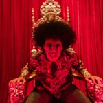 Dynamiczny portret młodego dorosłego na ozdobnym krześle w odważnym czerwonym pokoju.