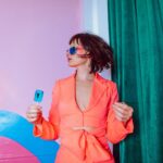 Tadź Mahal: Miłość zapisana w marmurze Modny portret przedstawiający kobietę w żywym stroju, w okularach przeciwsłonecznych, trzymającą niebieskiego lizaka.