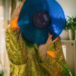 Sikkim: Duchowe i przyrodnicze bogactwo Himalajów Kobieta w złotej cekinowej kurtce trzymająca niebieską płytę winylową w pomieszczeniu, w klimacie retro