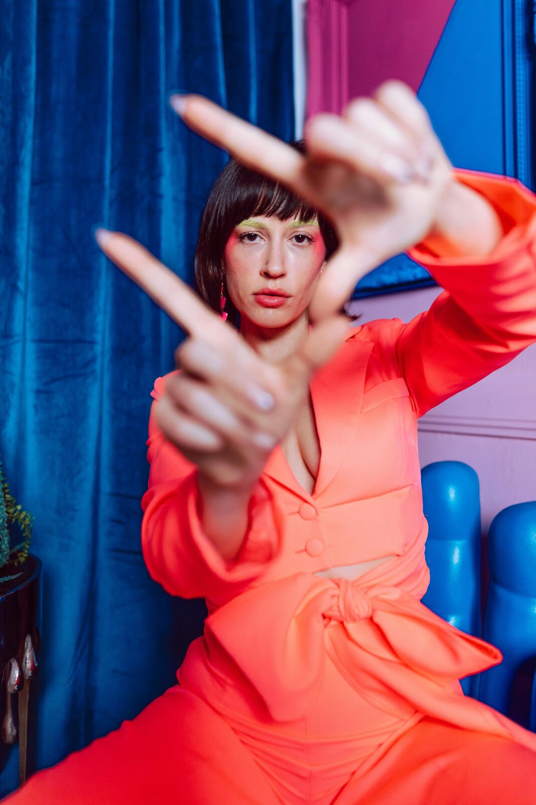 Kolorowy portret stylowej kobiety pozującej w pomieszczeniu na jaskrawo niebieskim i różowym tle.