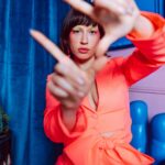 Mysuru (Mysore): Królewskie miasto i pałac maharadży Kolorowy portret stylowej kobiety pozującej w pomieszczeniu na jaskrawo niebieskim i różowym tle.