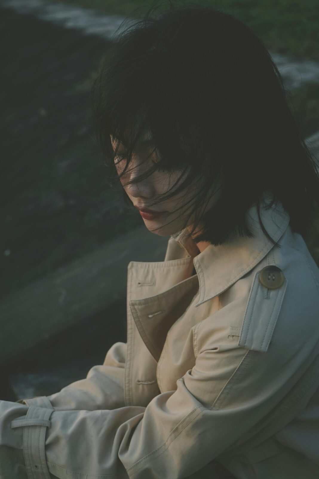 indie Spokojny portret kobiety w trenczu, siedzącej na zewnątrz z rozwianymi włosami.