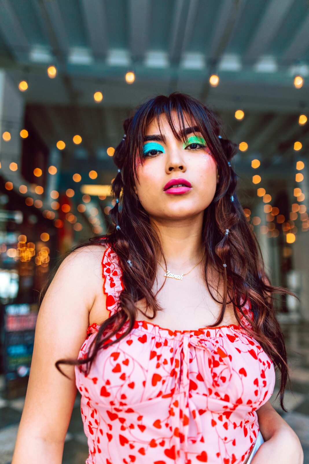 Stylowa kobieta z kolorowym makijażem i sukienką w serce w tętniącej życiem scenerii.