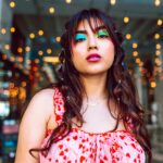 Stylowa kobieta z kolorowym makijażem i sukienką w serce w tętniącej życiem scenerii.