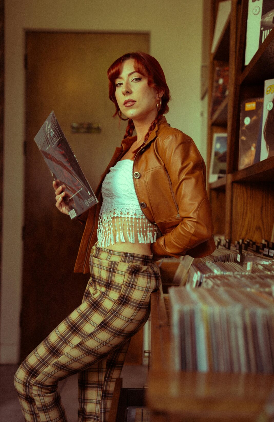 indie Stylowa kobieta z rudymi włosami przeglądająca płyty winylowe w sklepie z płytami retro.