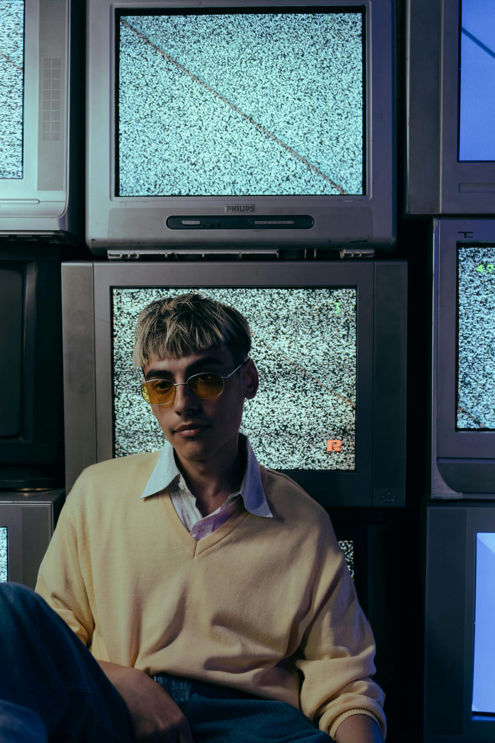 Stylowy nastolatek pozuje przed zabytkowymi telewizorami CRT z szumem statycznym.
