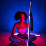 Kreatywny portret kobiety siedzącej przy neonach, prezentujący żywe kolory i nowoczesny styl.