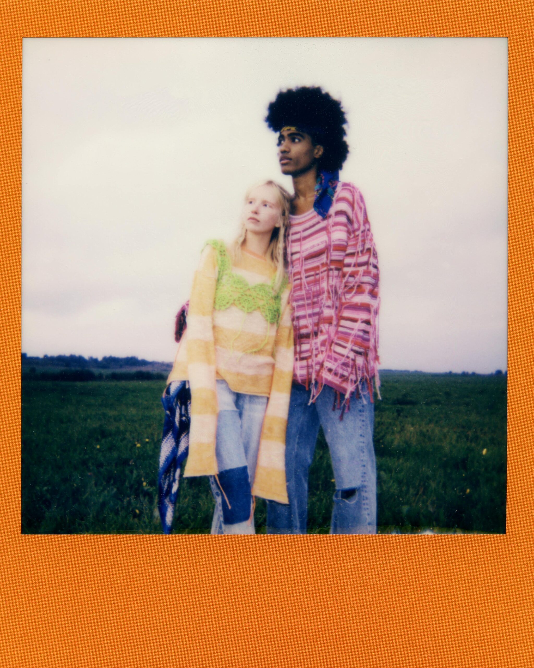 Młoda para w kolorowych ubraniach w stylu bohemy obejmująca się na wiejskiej łące.