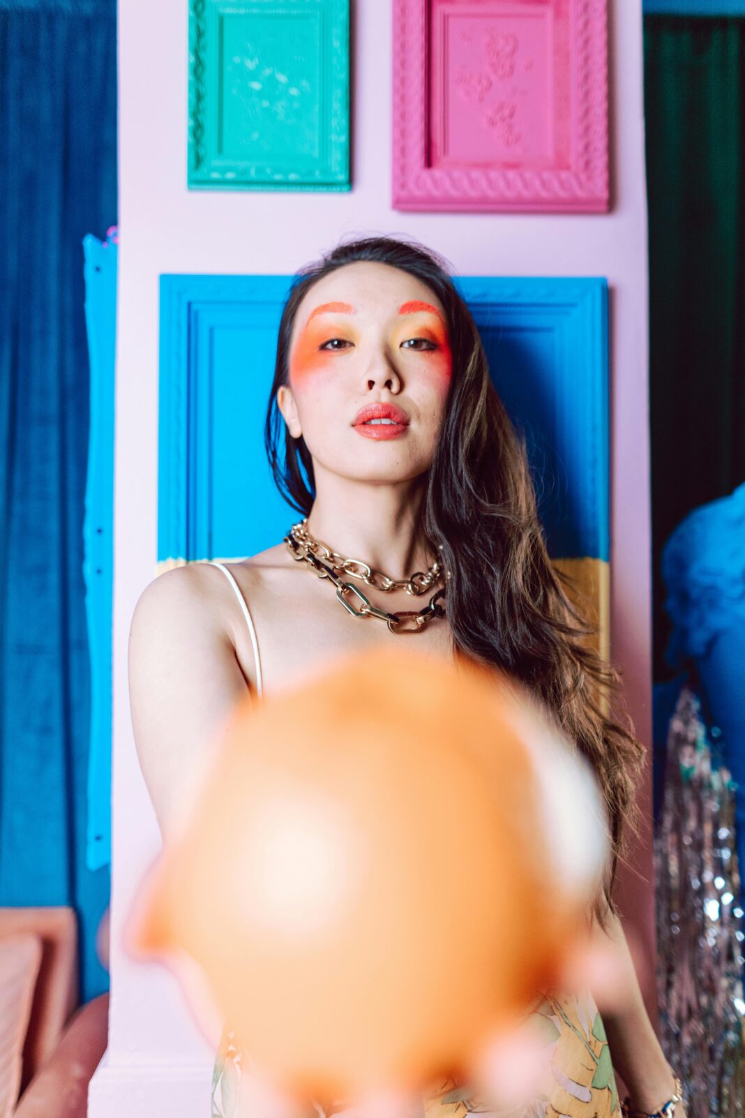 Stylowy portret kobiety z odważnym makijażem i kolorowym tłem.