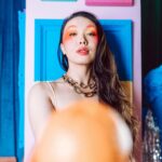 Stylowy portret kobiety z odważnym makijażem i kolorowym tłem.