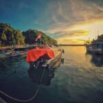 Oszałamiający widok na zachód słońca w porcie Girisubo w Indonezji, z łodziami i bujnymi wzgórzami.