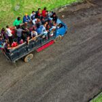 Zdjęcie lotnicze przedstawiające ciężarówkę pełną ludzi podróżujących po wiejskiej drodze w Indonezji.