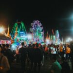 Zatłoczona wieczorna scena oświetlonego karnawału z diabelskimi kołami i żywymi światłami.