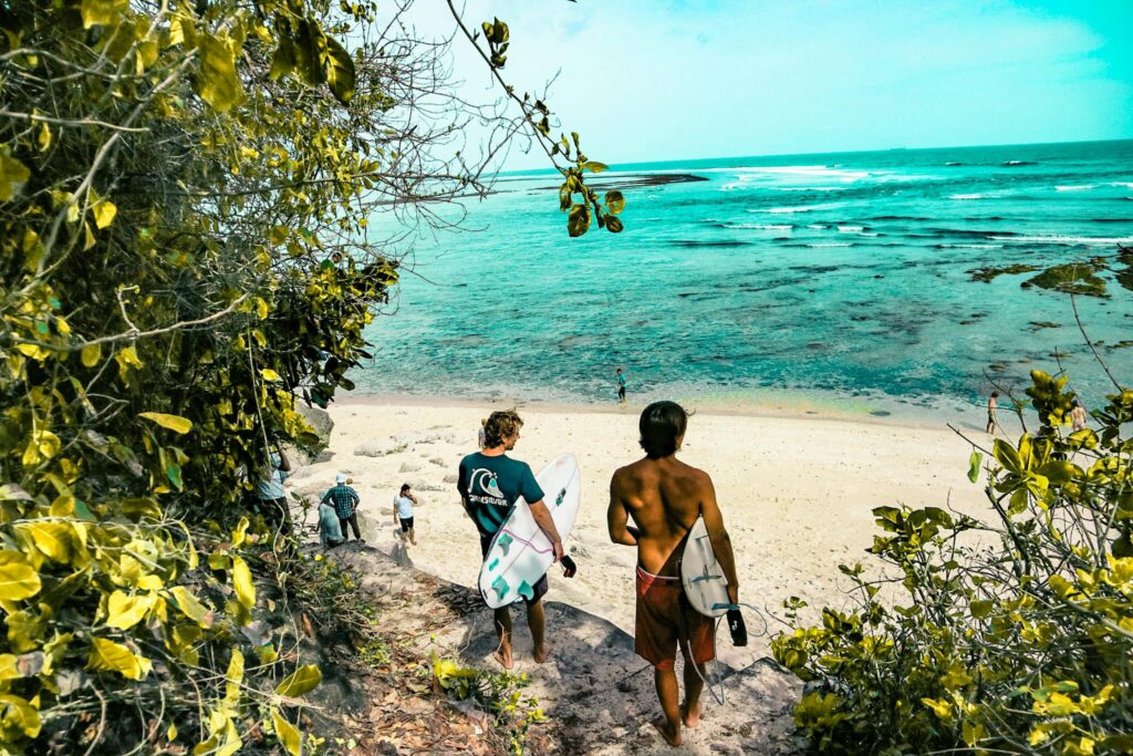 Surferzy udają się bujną ścieżką na oszałamiającą plażę na Bali w Indonezji.
