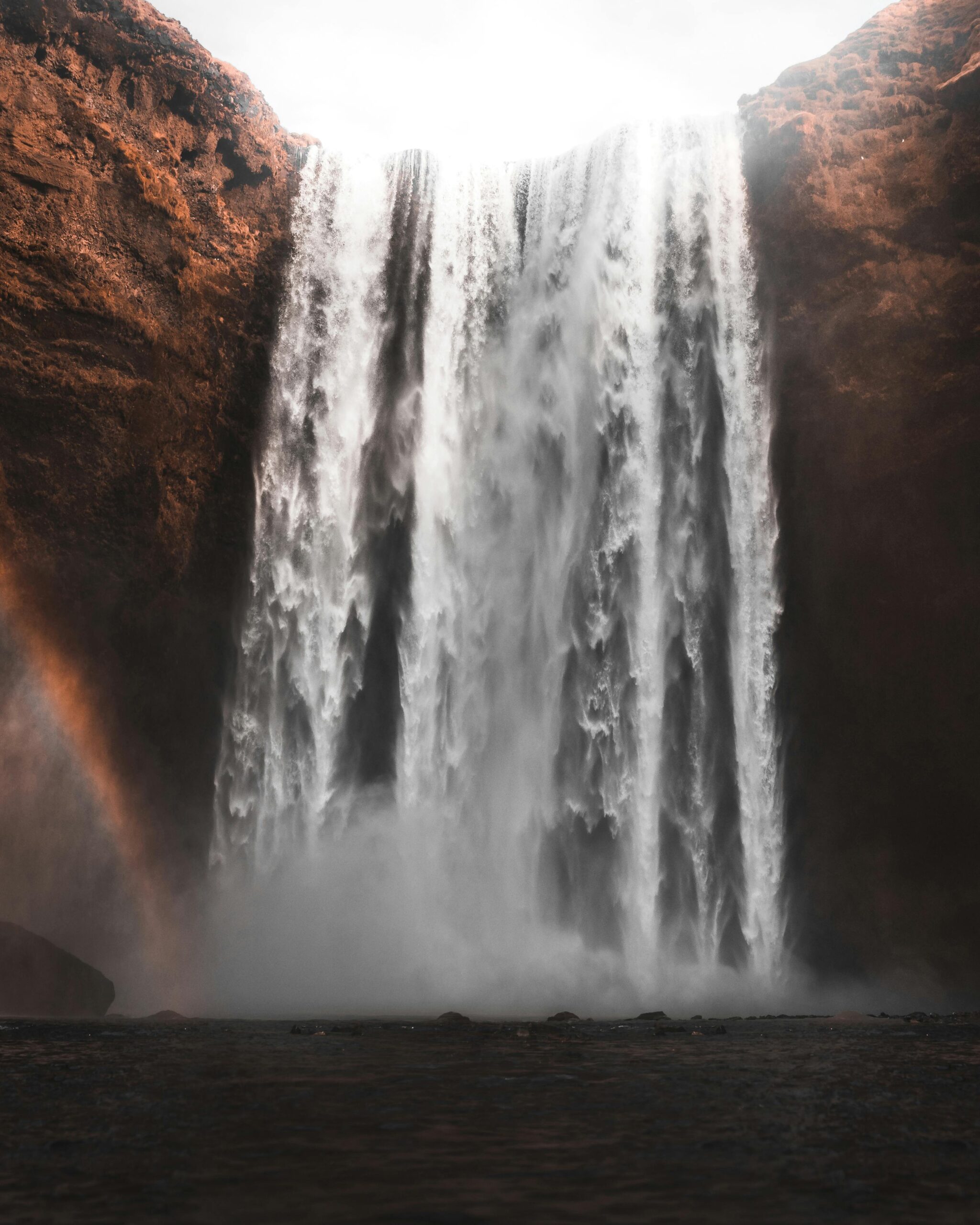 Piękny widok na wodospad Skogafoss spływający kaskadą po klifach na Islandii z łukiem tęczy obok.