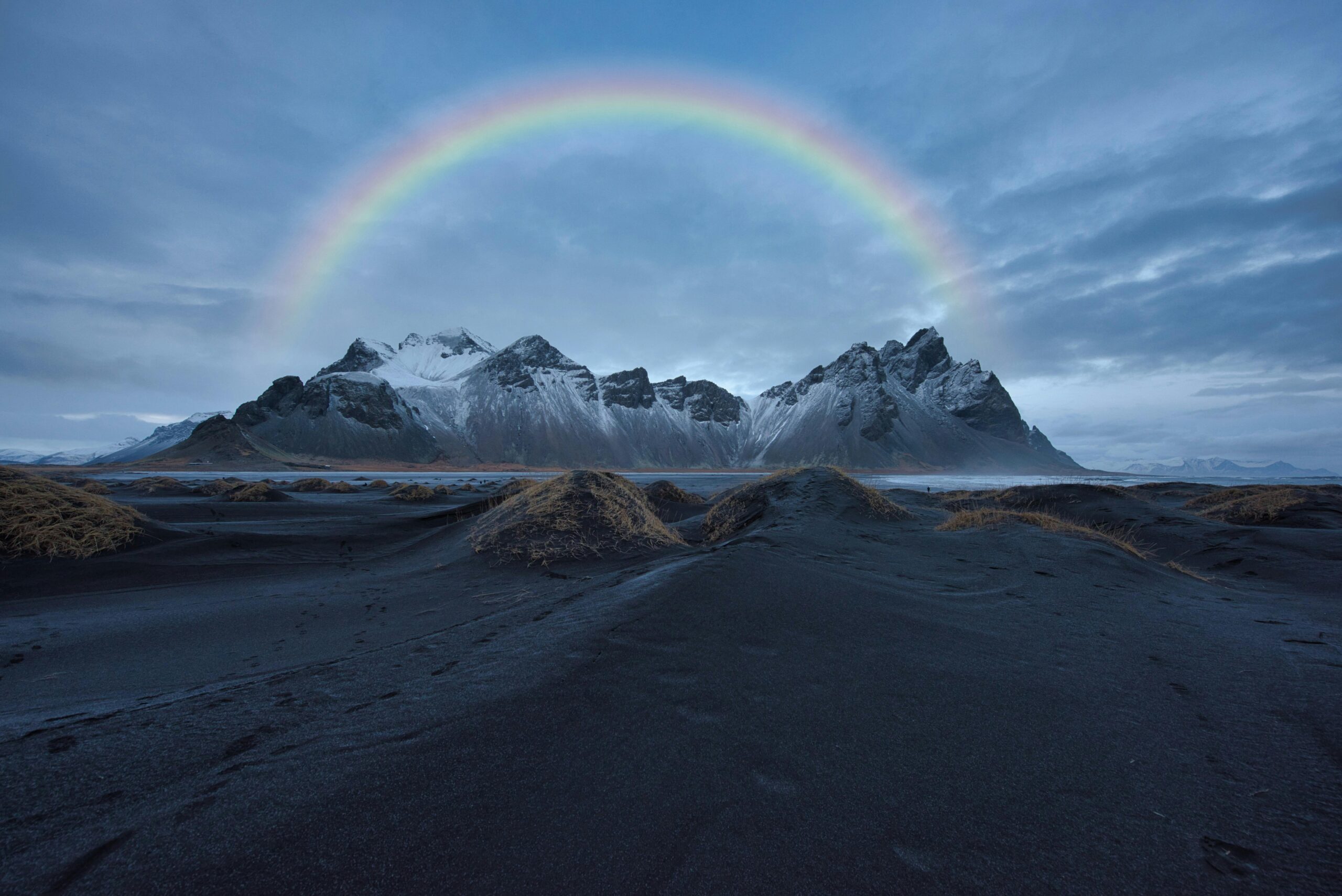 Oszałamiający widok na górę Vestrahorn z żywą tęczą wyginającą się nad czarną piaszczystą plażą na Islandii.