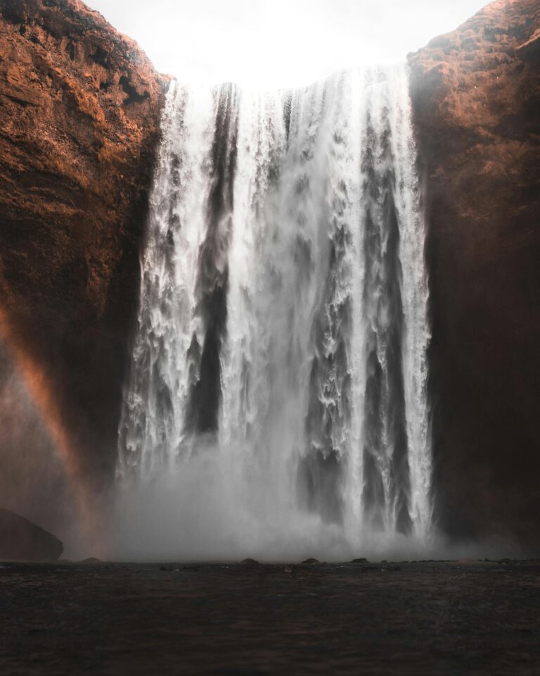 Piękny widok na wodospad Skogafoss spływający kaskadą po klifach na Islandii z łukiem tęczy obok.