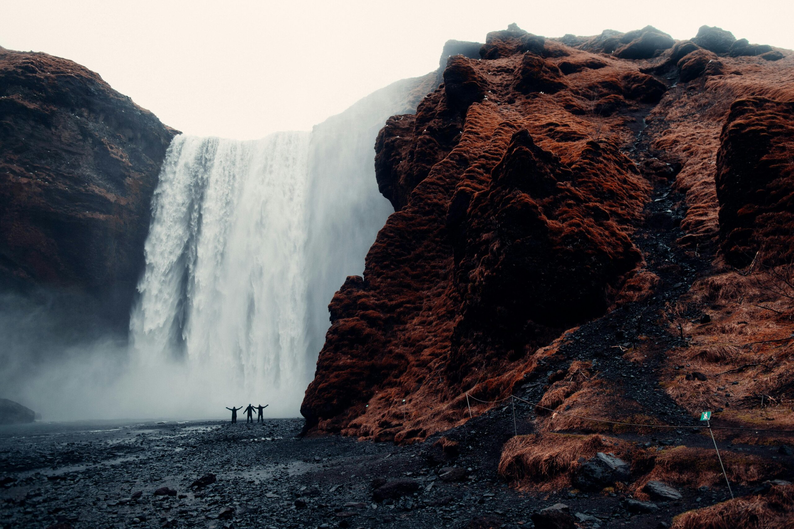 Grupa poszukiwaczy przygód stoi przed majestatycznym wodospadem Skogafoss na Islandii.