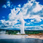 Islandia – ciekawostki o Reykjaviku Oszałamiająca erupcja gejzeru pod tętniącym życiem błękitnym niebem z dramatycznymi chmurami w malowniczym krajobrazie Islandii.