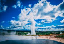 Islandia – ciekawostki o Reykjaviku Oszałamiająca erupcja gejzeru pod tętniącym życiem błękitnym niebem z dramatycznymi chmurami w malowniczym krajobrazie Islandii.