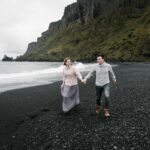 Islandia – najpiękniejsze miejsca na trekking Szczęśliwa kochająca para trzymająca się za ręce i odkrywająca wspaniałą czarną żwirową plażę, ciesząc się weekendem na klifowym wybrzeżu