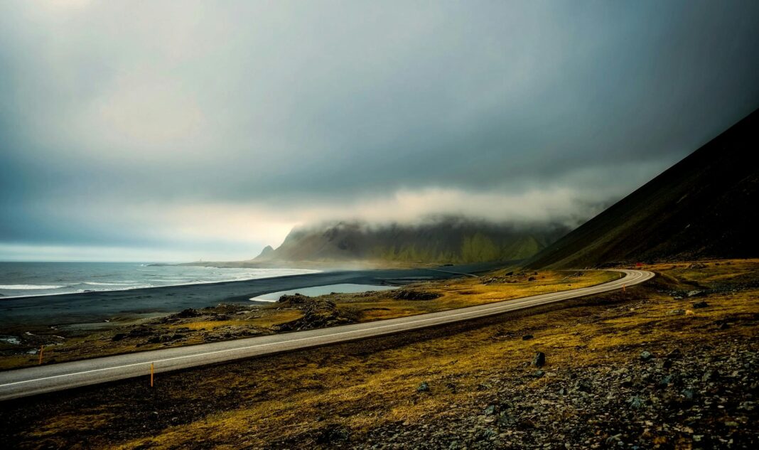 islandia Dramatyczny krajobraz przybrzeżny z krętą drogą i pochmurnym niebem na Islandii.