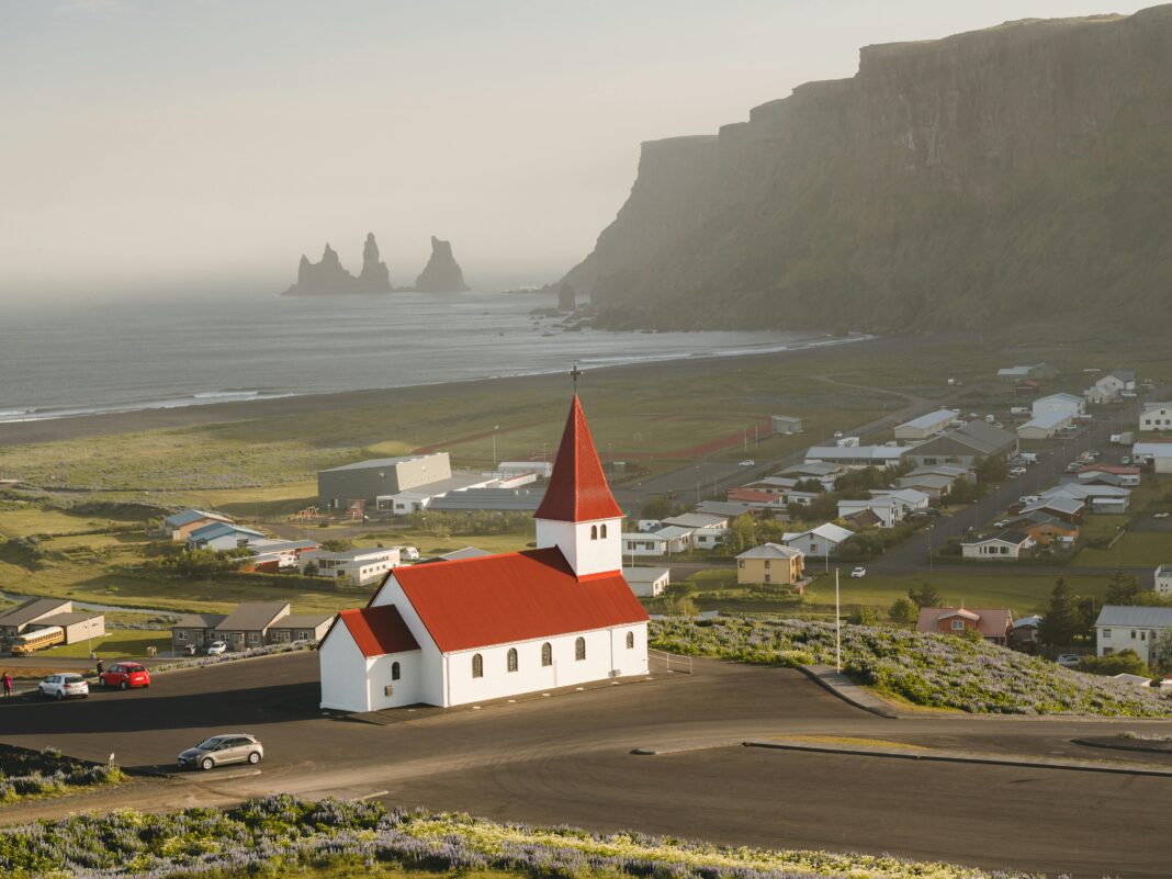 Widok z lotu ptaka na kultowy kościół Vik z czerwonym dachem i kominami Reynisdrangar wzdłuż wspaniałego islandzkiego wybrzeża.