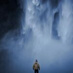 Samotny mężczyzna patrzy na majestatyczny wodospad na Islandii, spowity mgłą.