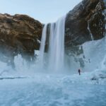 Islandia – przewodnik dla miłośników natury Zapierający dech w piersiach widok na wysoki wodospad pośród lodowych krajobrazów na Islandii.