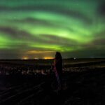 Sylwetka kobiety podziwiającej zorzę polarną na nocnym niebie Islandii.