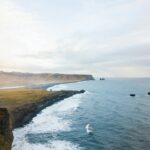 Islandia – czy warto wybrać się na wycieczkę objazdową? Zapierający dech w piersiach widok z lotu ptaka na skaliste przybrzeżne klify Islandii i rozległy ocean pod zachmurzonym niebem.